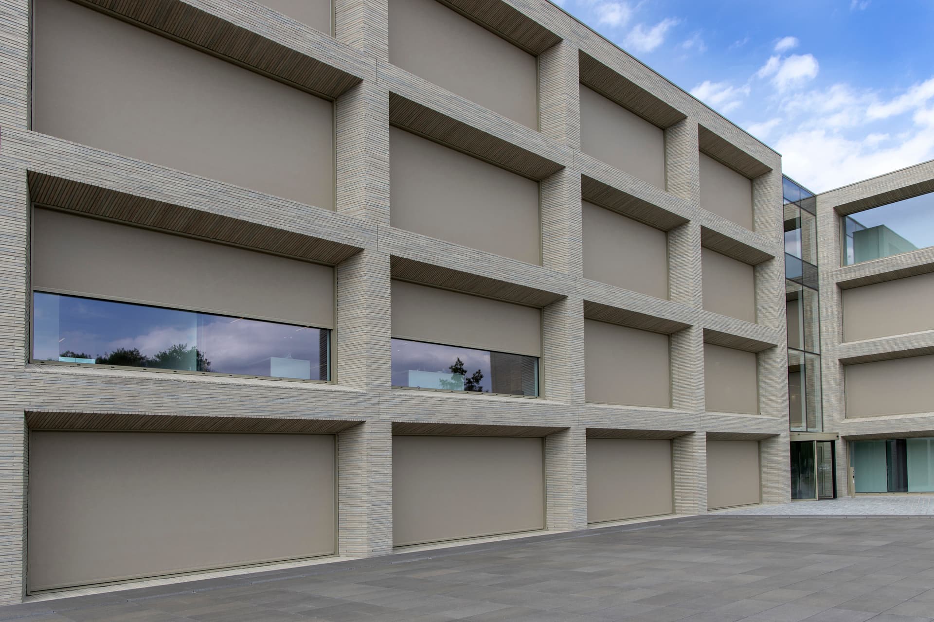 Windvaste Brustor outdoor ZIP‑screens die de ramen van een modern kantoorgebouw volledig afschermen voor optimale zonwering en privacy