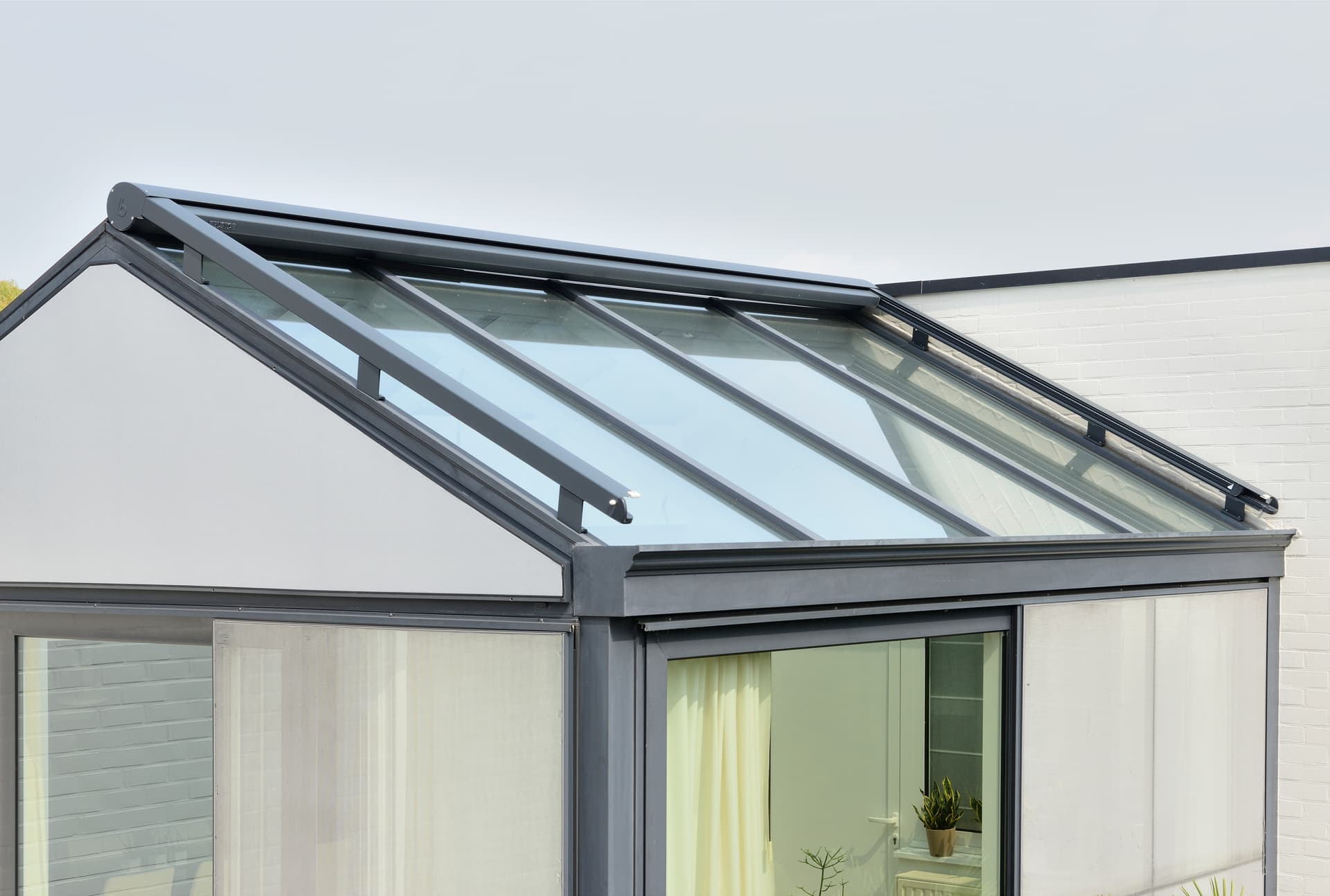 Brustor B126 conservatory awning in retracted position mounted above a sloped glass veranda roof for exterior sun protection