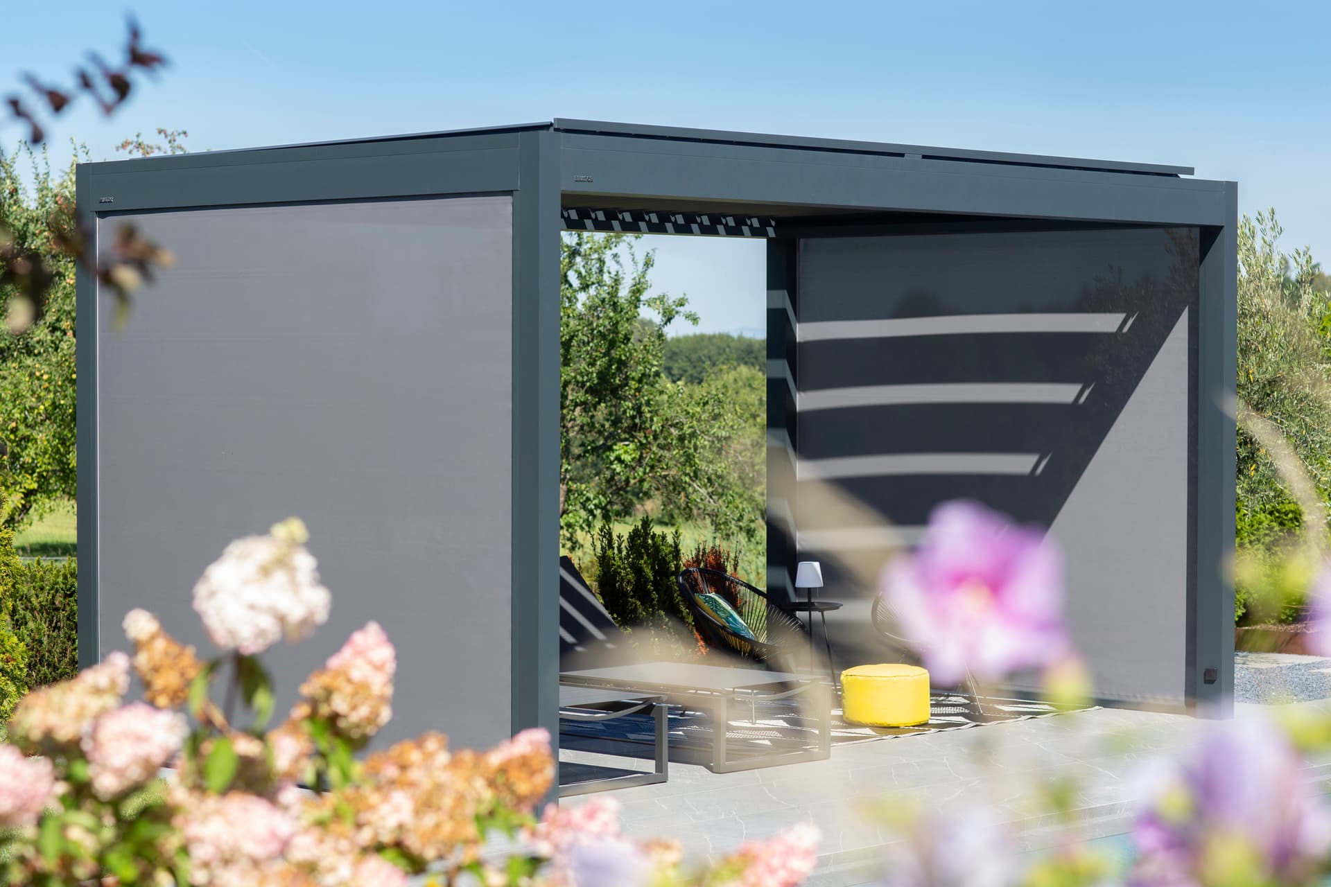 Pergola Brustor con lamelle orientabili, illuminazione LED integrata, screen ZIP e riscaldatori da terrazza che creano una zona pranzo esterna protetta