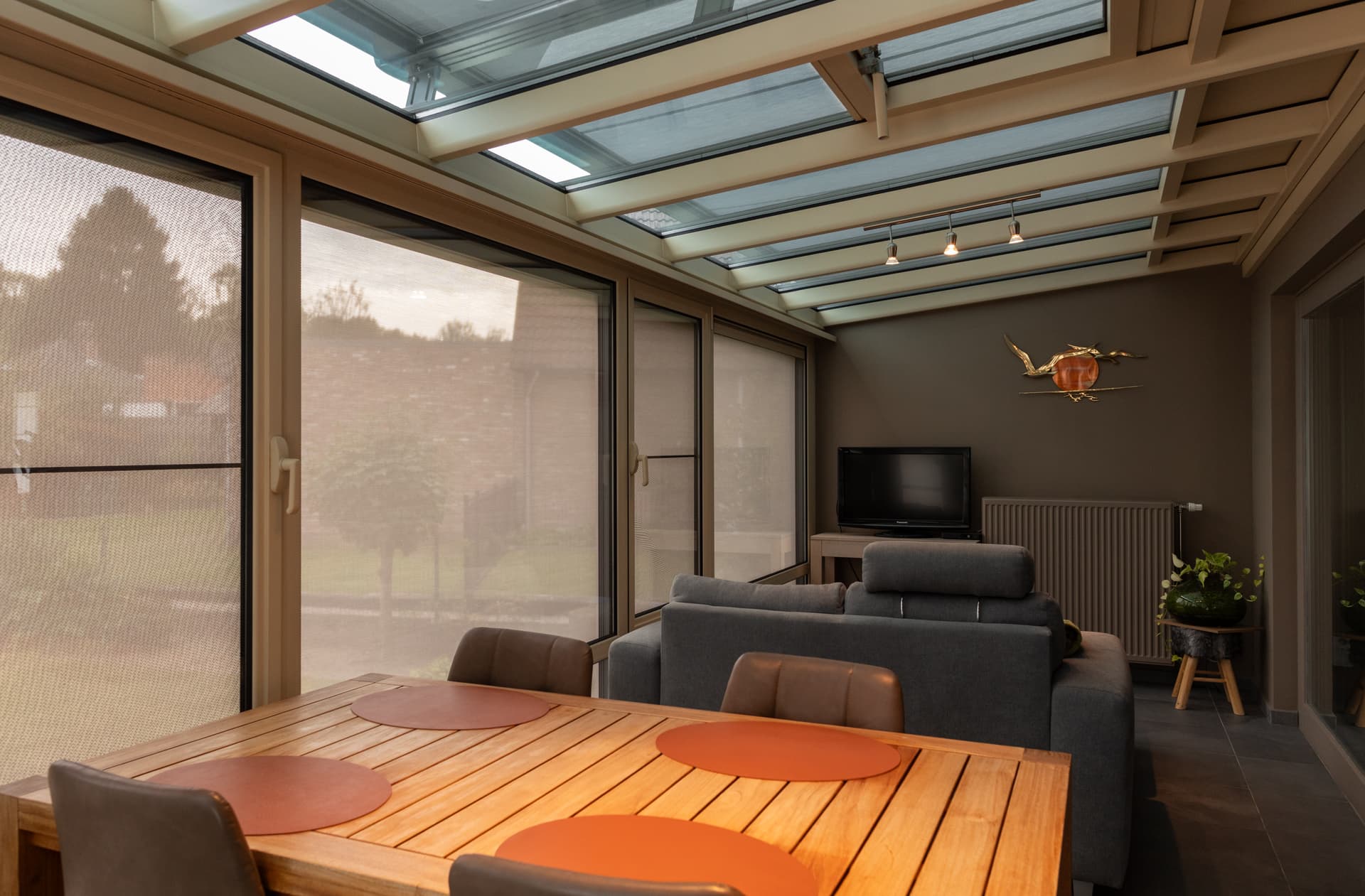 Brustor B126 under‑glass awning filtering sunlight beneath a glass veranda roof, creating a comfortable indoor seating and dining area